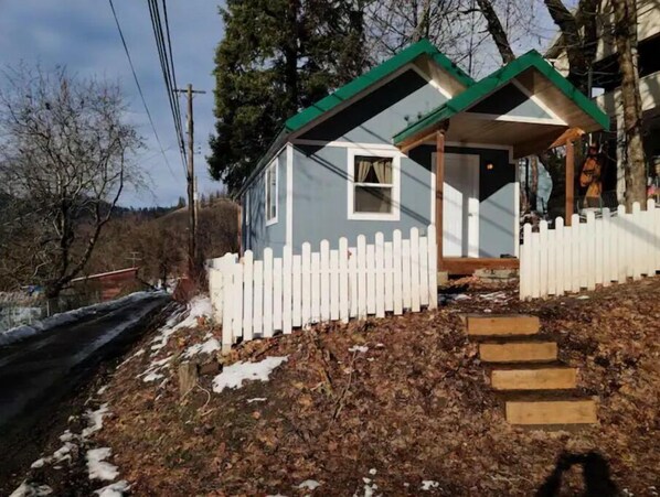 Situated on a sloped terrain, this charming house features a white picket fence and a wooden staircase leading up to the entrance.