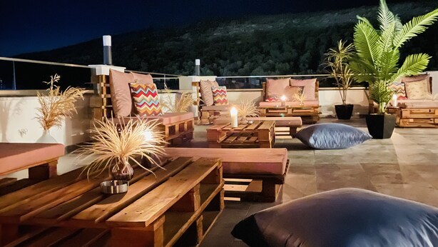 Eine Dachterrasse mit Holzmöbeln, Kissen und Blumentöpfen.