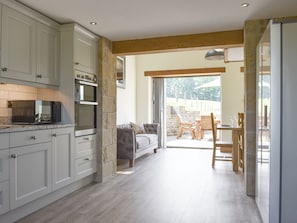 A kitchen with built-in appliances, a dining area with a table and chairs, and a view through a glass door to an outdoor space. - 4 bedroom accommodation in Harkerside, near Grinton (Harkerside, near Grinton)