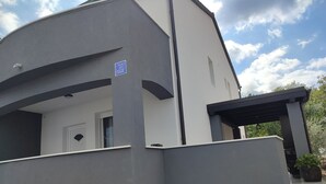 A modern building with a grey facade, a covered outdoor area, and a visible door. - Villa Ivka with Swimming Pool (Dobrinj)