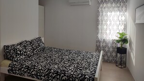 A bedroom with a bed, a window with patterned curtains, a potted plant, and an air conditioning unit. - Villa Ivka with Swimming Pool (Dobrinj)