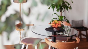 Une table ronde en verre, sur laquelle se trouve un saladier rempli de fruits, un téléphone intelligent et une chaise dotée d’un siège rembourré.