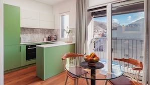 Une cuisine moderne avec des meubles de couleur verte, un pare-feu en marbre et un coin repas comprenant une table et des chaises en verre.