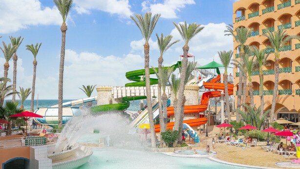 A water park with multiple slides and a pool area, surrounded by palm trees and a building with balconies. - Hotel Marabout - Families and Couples Only (Sousse)