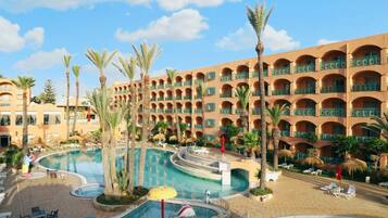 A resort with a large central pool, palm trees, and a multi-story building with balconies.