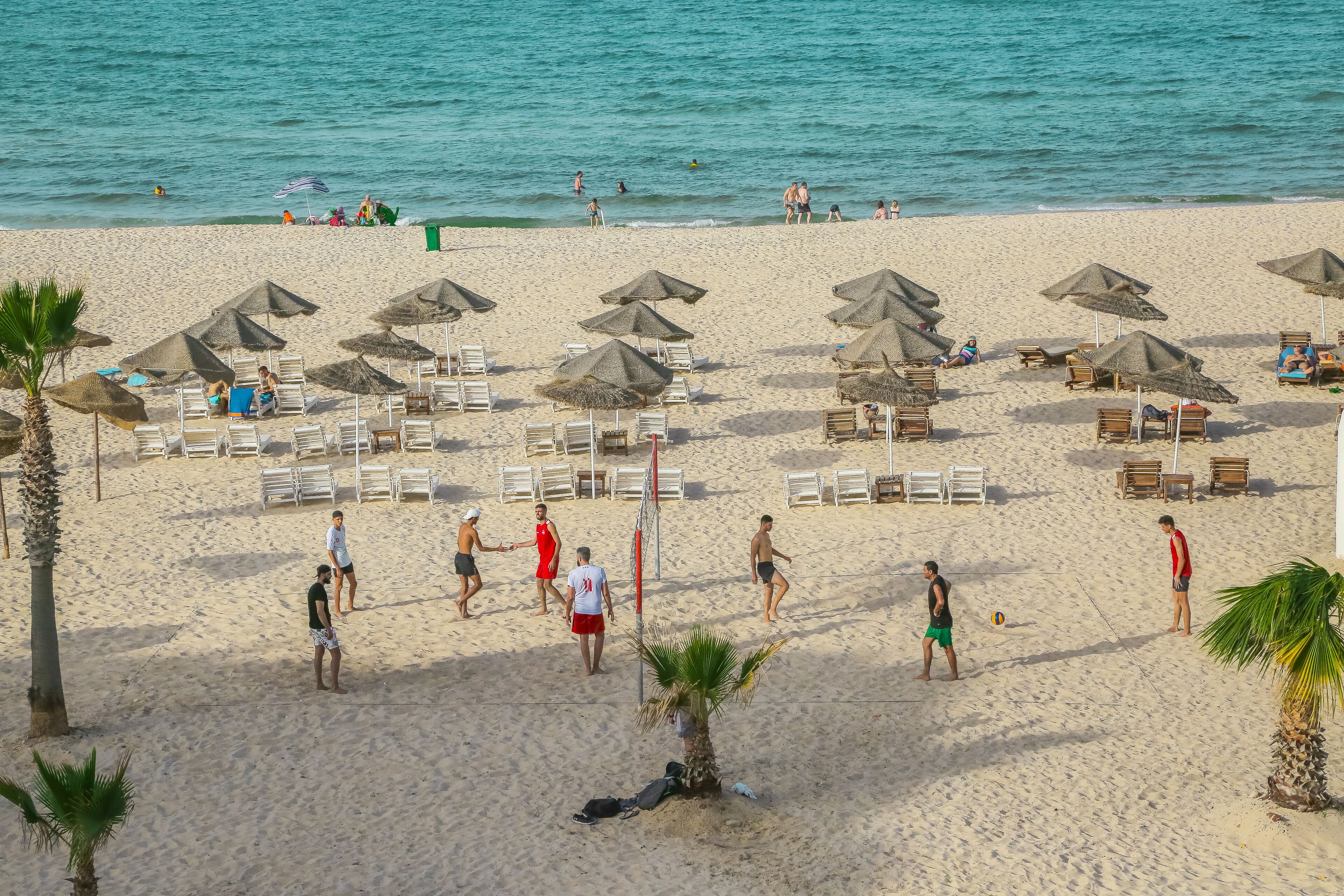 Een strand met ligbedden, parasols en een volleybalnet.