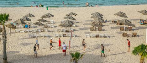 Une plage avec des transats, des parasols et un filet de volley-ball.