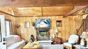 Un salon chaleureux avec des murs et un plafond en bois, une cheminée, un canapé, une table basse et un téléviseur.