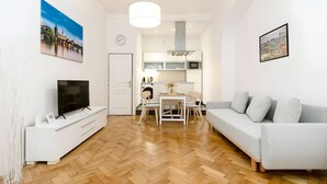 Una sala de estar moderna con televisor de pantalla plana, un sofá, una zona de comedor con mesa y sillas, y una cocina con microondas y estufa.