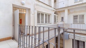 Un edificio residencial de varios pisos con balcones, un detector de incendios visible y una entrada con portón.