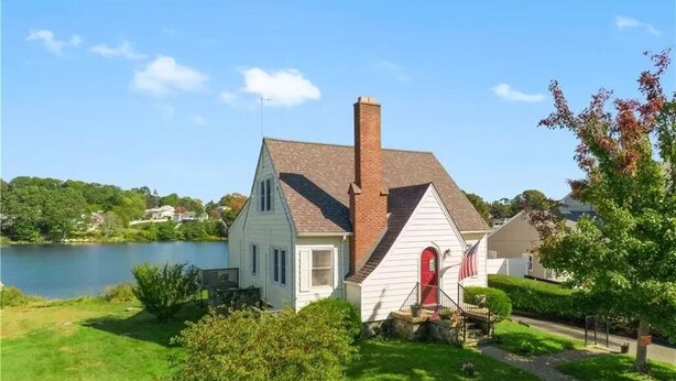 A two-story house with a red door, a chimney, and a view of a lake. - Waterfront Cottage within walking distance to the Beach. A dog-friendly property (Waterford)