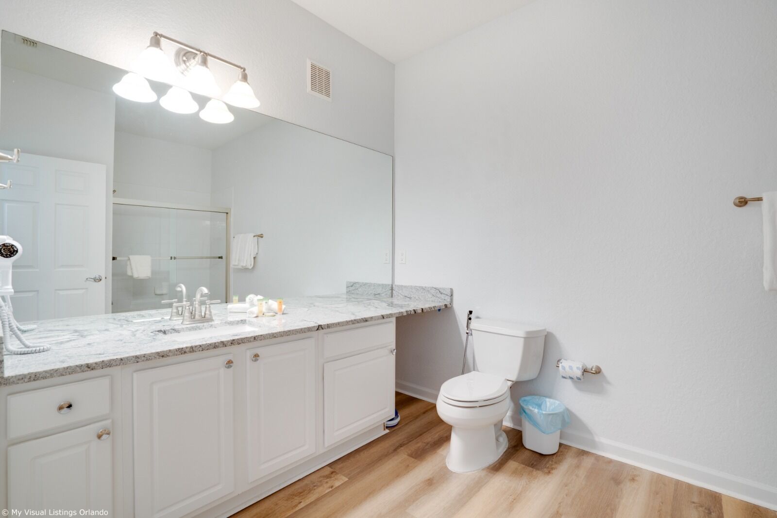 Une salle de bain avec un meuble-lavabo blanc, un grand miroir, des toilettes et une poubelle.