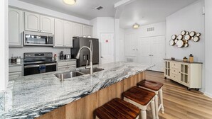 A modern kitchen with white cabinets, a granite countertop, and a built-in island with stools. - VISTA CAY RESORT (Orlando)