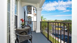 A balcony with wicker furniture, a potted plant, and a view of a parking lot and distant buildings. - VISTA CAY RESORT (Orlando)