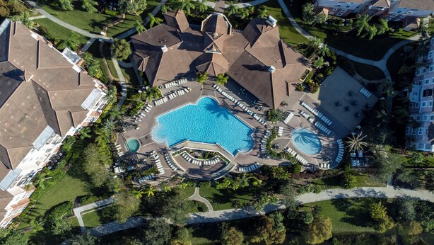An aerial view of a resort with a central swimming pool, multiple lounge areas, and a variety of buildings with distinct architectural styles. - VISTA CAY RESORT (Orlando)