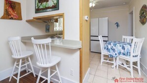 Une cuisine avec des meubles blancs, un coin repas comprenant une table et des chaises, et un réfrigérateur à l’arrière-plan.