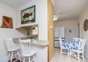 A kitchen with white cabinetry, a dining area with a table and chairs, and a refrigerator in the background.