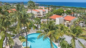 A resort with a large swimming pool surrounded by palm trees and a view of the ocean. - Beautiful luxury apartment with panoramic views of the Caribbean Sea (Willemstad)