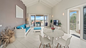 A spacious living area with a high ceiling, a white sofa with blue cushions, a round dining table with chairs, and a view through a glass door to the outside. - Beautiful luxury apartment with panoramic views of the Caribbean Sea (Willemstad)