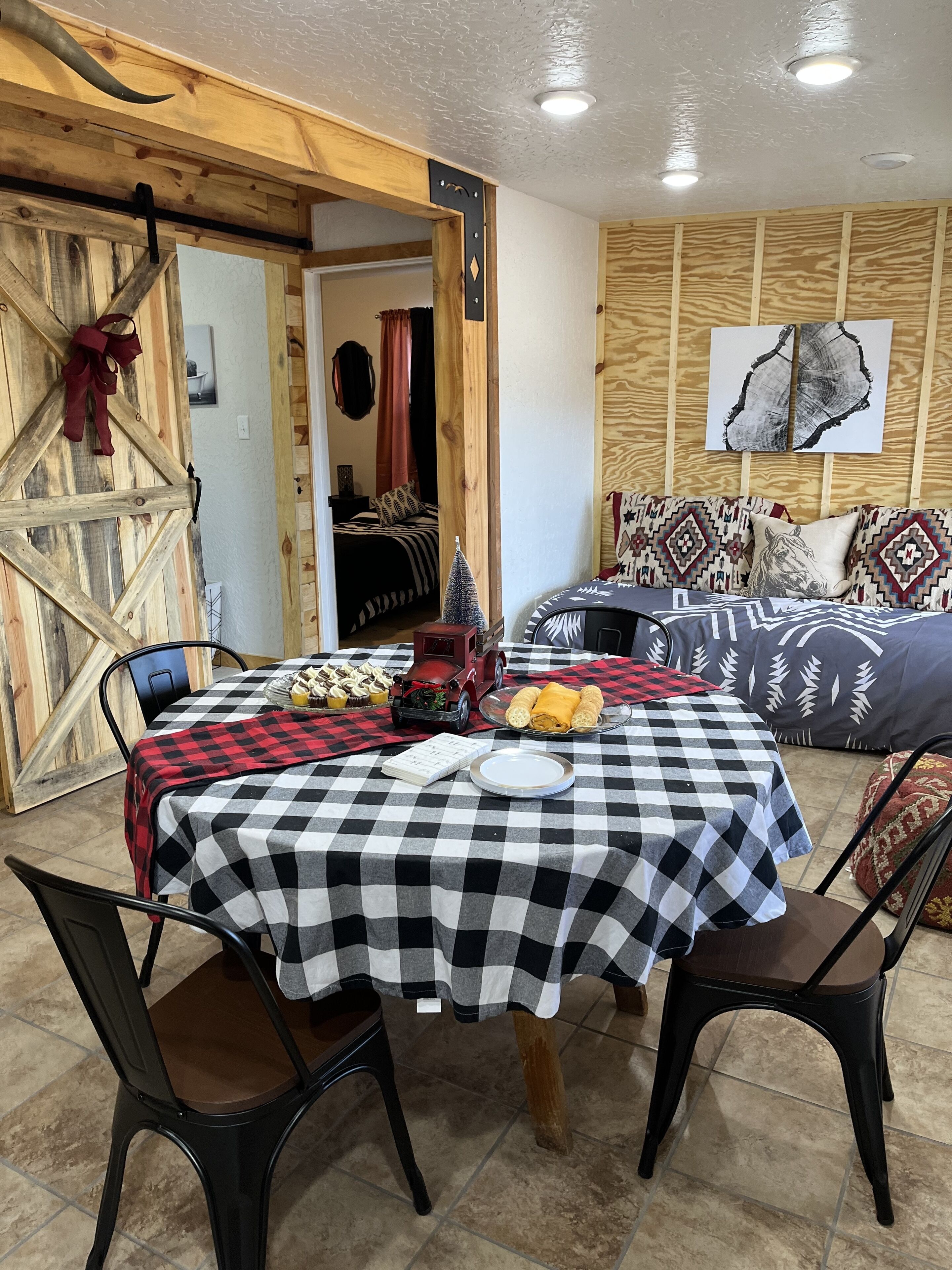 Una habitación acogedora con una mesa de cuadros, una cama con almohadones estampados y una puerta de madera rústica.