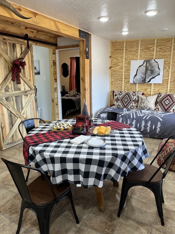 A cozy room with a checkered table, a bed with patterned pillows, and a rustic wooden door.