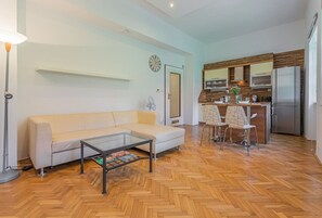 Una sala de estar moderna con sofá, mesa de centro y una zona de cocina con refrigerador, microondas y mesa de comedor con sillas.