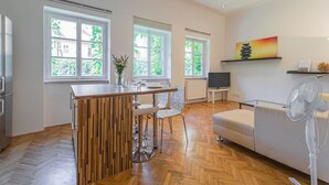 Une cuisine moderne avec un îlot central en bois, un coin repas avec des chaises, un canapé, une télévision et un ventilateur.