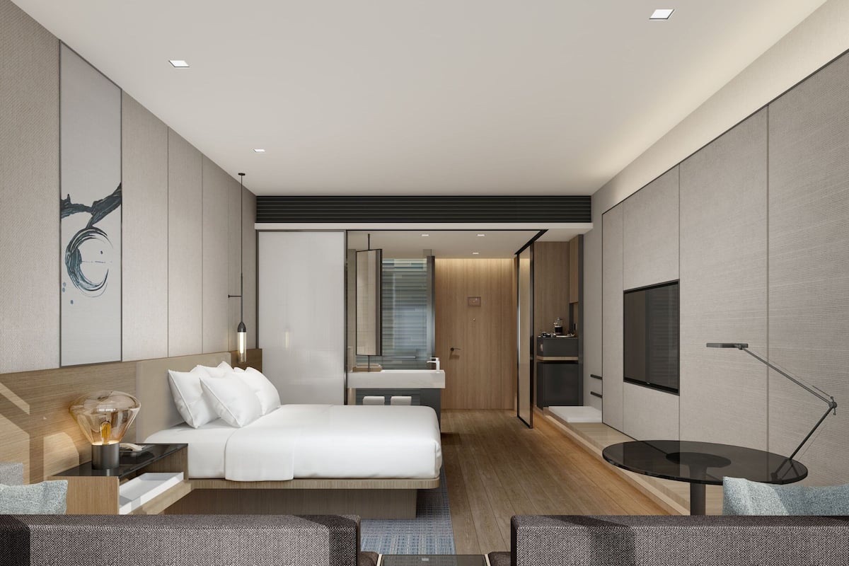 A modern hotel room with a bed, bedside table, lamp, TV, and a view of the bathroom.