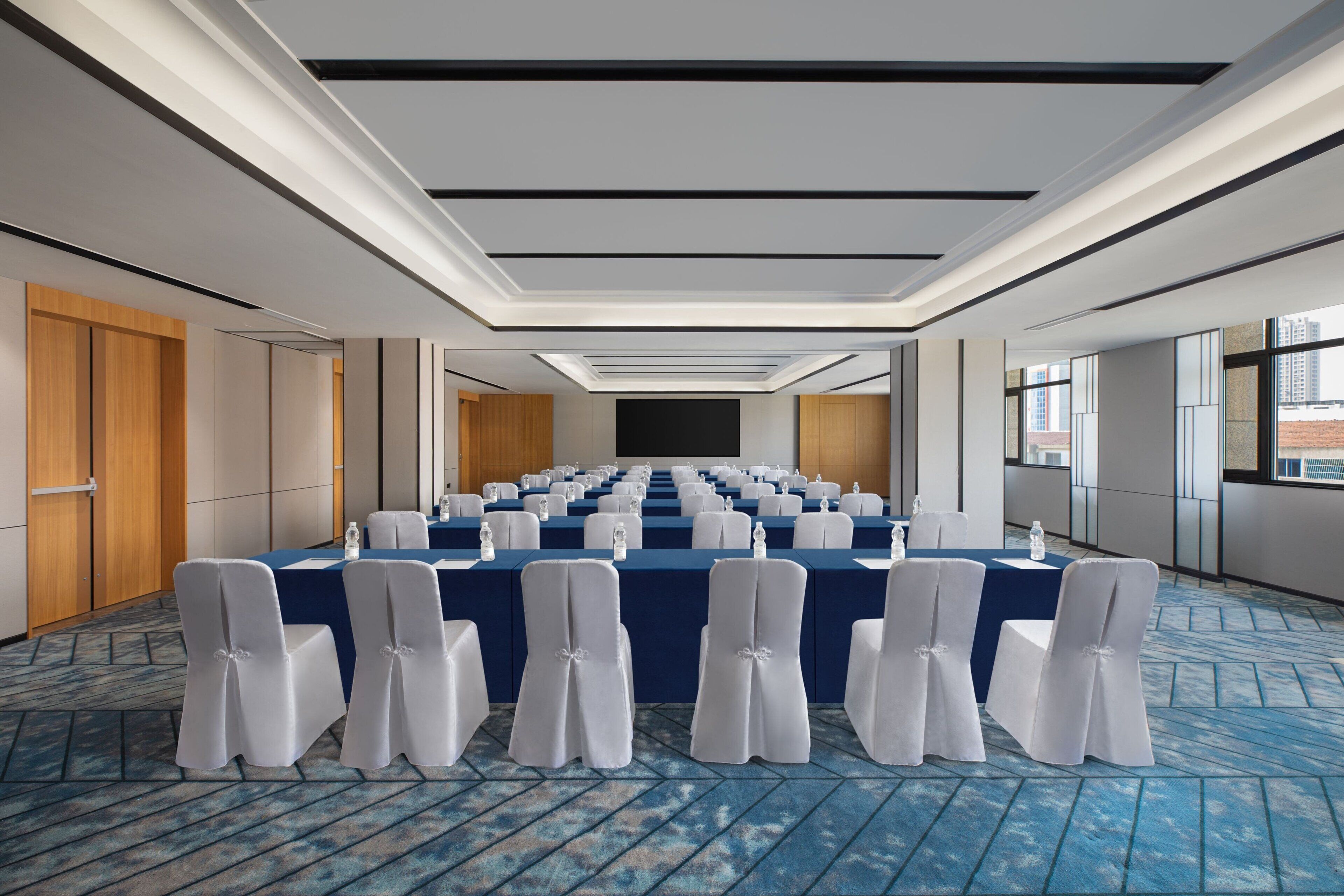 A conference room with a long table, white chairs, and a blue carpet.