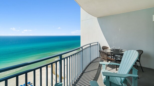 A balcony with a view of the ocean, a table with chairs, and a small table with a bottle and glasses. - Sterling Breeze 1205 - Gulf Front Condo (Panama City Beach)