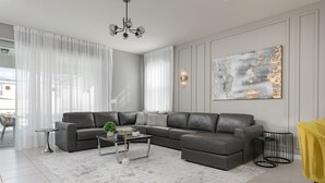 Ein modernes Wohnzimmer mit einem grauen Ecksofa, einem Couchtisch und einem großen, abstrakten Gemälde an der Wand.