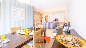 A dining area with a wooden table set for breakfast, a sofa, and a TV in the background. - #115 Bernardo Flat by Home Holidays (Albufeira)