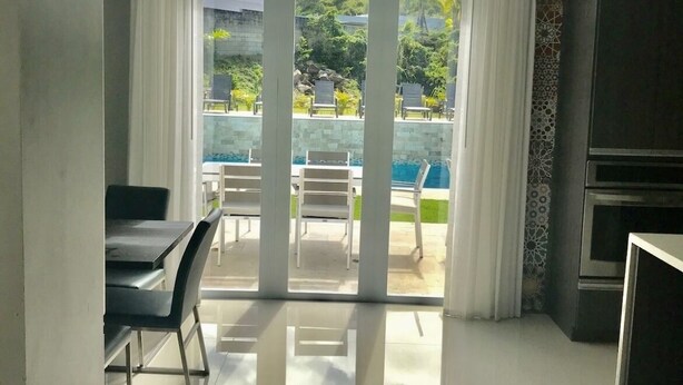 Et moderne køkken med en stor ø, et spiseområde med stole, samt udsigt til et poolområde udendørs.
