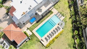 Ovenudblik over et stort, moderne hus med swimmingpool, overdækket terrasse og velanlagt have.