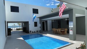 Ein moderner Poolbereich im Freien mit freiem Blick auf den Ozean, einer überdachten Lounge und einer amerikanischen Flagge.