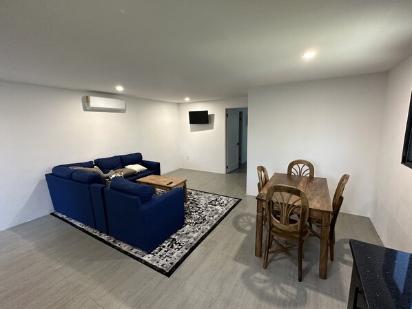Ein modernes Wohnzimmer mit einem blauen Sofa, einem Holzesstisch mit Stühlen und einem gemusterten Teppich.