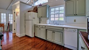Una cocina con armarios blancos, piso de madera, lavavajillas integrado y ventana con vistas a árboles.