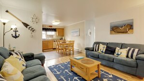 Ein Wohnzimmer mit grauem Sofa, einem Holztisch und einem blauen Teppich mit Anker-Muster.