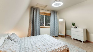 Une chambre à coucher comprenant un lit, une commode, un grand miroir et une fenêtre avec des rideaux.