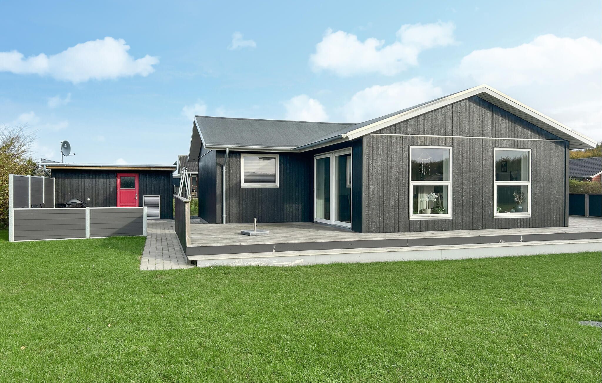 Une maison moderne à deux étages, avec une façade sombre, de grandes fenêtres et une porte rouge.