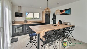 A modern kitchen with a wooden table and chairs, a built-in oven, and a large window. - Le 26 - Erdeven - Gîte (ERDEVEN)
