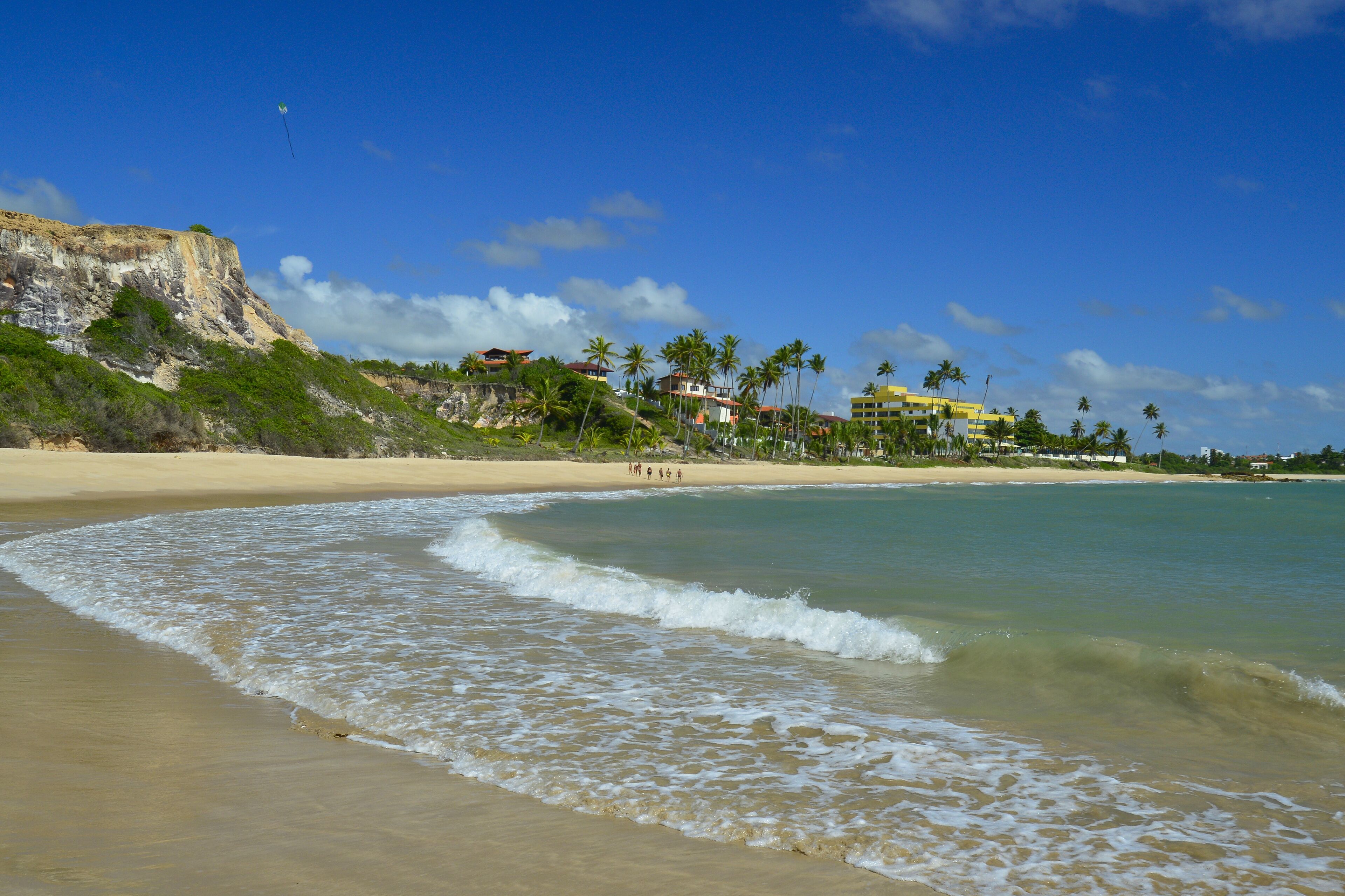 A beach with clear waters, a sandy shore, and buildings in the background.