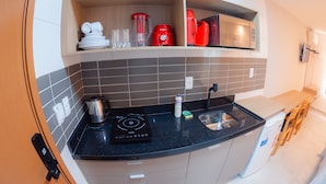 A compact kitchen with a black countertop, a built-in microwave, a red coffee maker, and a kettle. - Chocolate com Pimenta Edifício (João Pessoa)