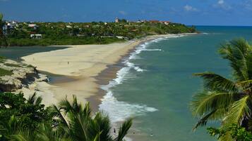 A beach with clear turquoise water, a sandy shore, and a backdrop of houses and greenery.