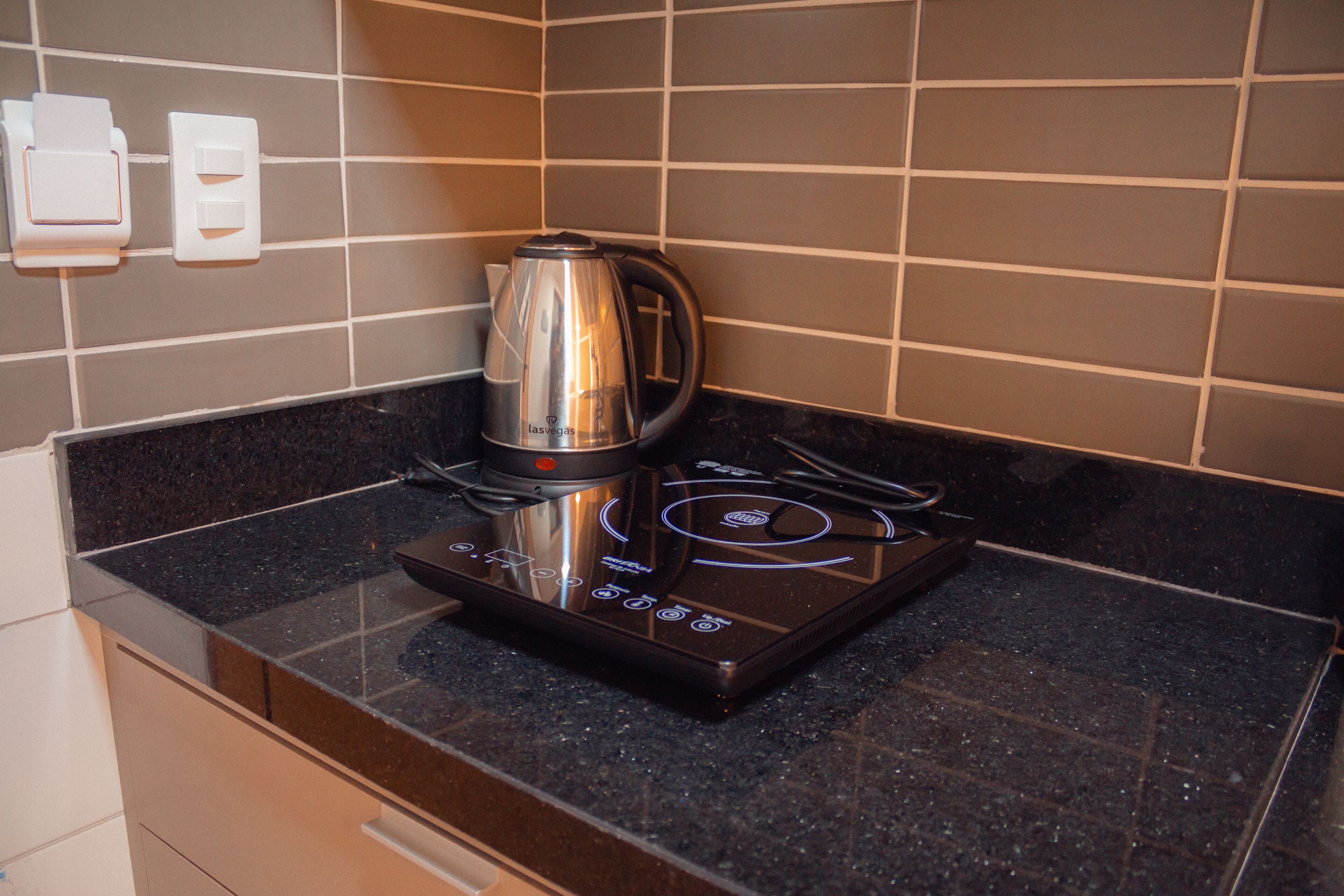 Uma cozinha com bancada preta, chaleira de aço inoxidável e fogão por indução embutido.
