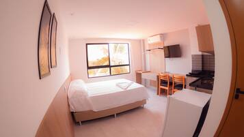 Een kleine kamer met een bed, een bureau, een stoel en een kitchenette.