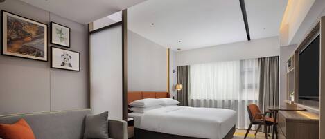A modern hotel room with a bed, sofa, desk, and TV.