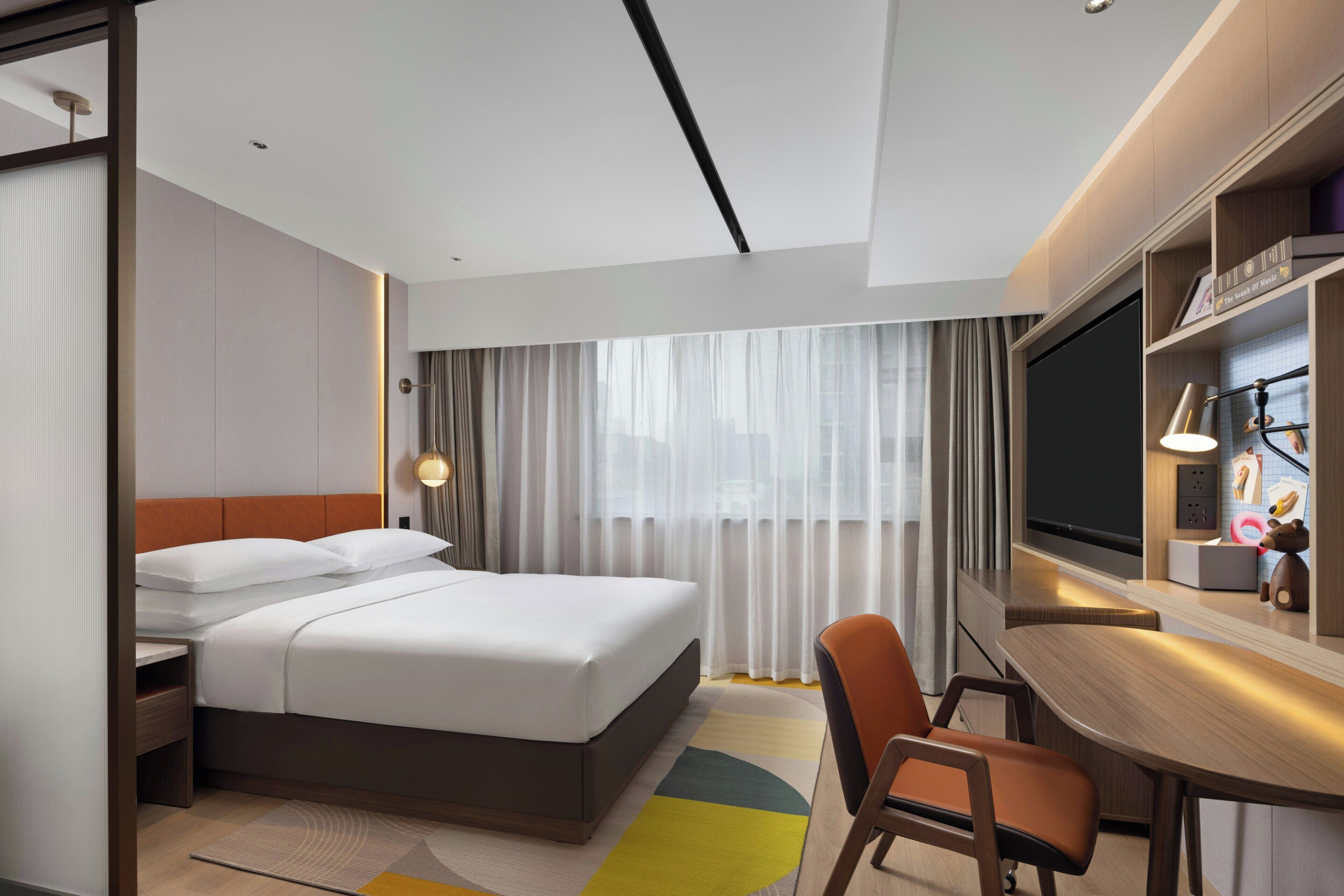 Ein Hotelzimmer mit Bett, Schreibtisch, Stuhl, Fernseher und einem Fenster mit Vorhängen.