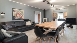 A modern living room with a black leather sofa, a wooden dining table with chairs, a large abstract painting, and a television.