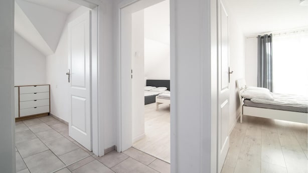 A bedroom with a bed, a bedside table, and a chair. There is a door leading to another room.